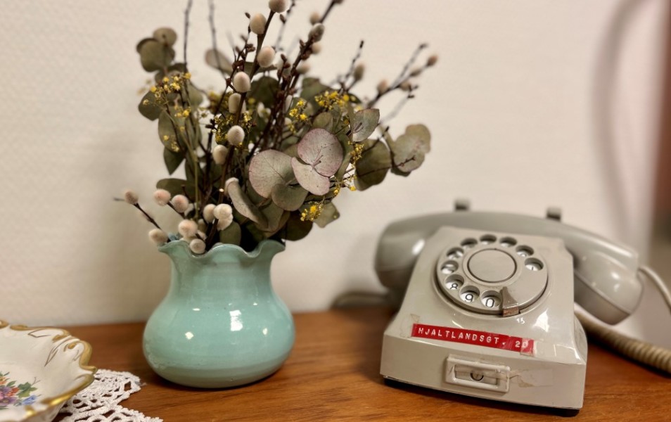 Bildet viser en vase og en gammel grå fasttelefon som står utsilt på en benk i gangen. De er flinke til å pynte.