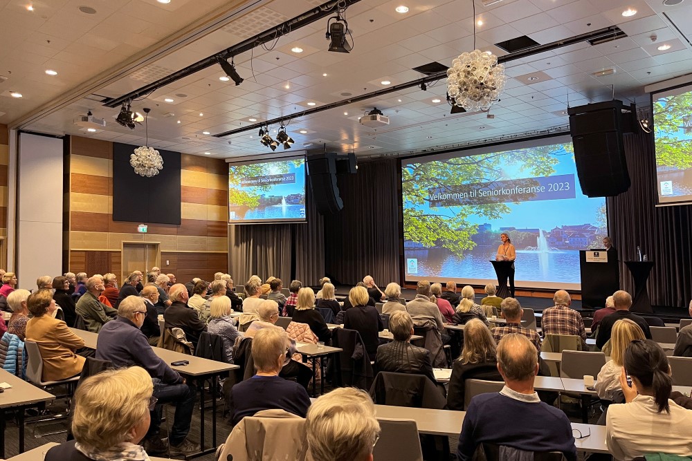 Bildet viser konferansesalen med mange mennesker som følger med på åpningen av Seniorkonferansen 2023 som skjer fra scenen. 