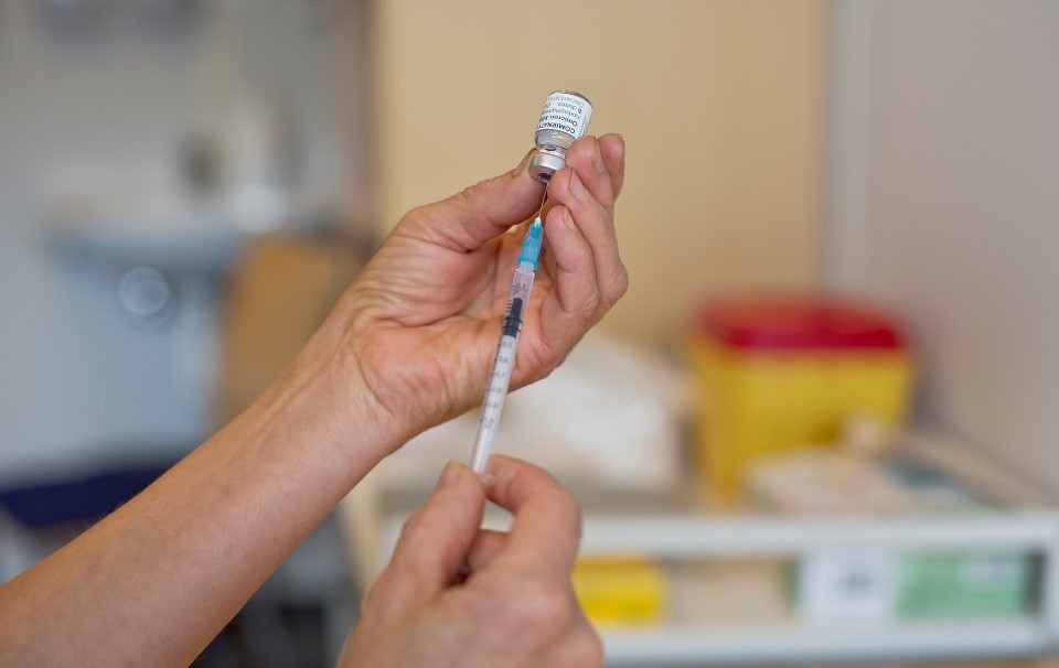 Bildet viser hendene til en sykepleier som trekker ut vaksine av en ampull med en sprøyte på vaksinekontoret.
