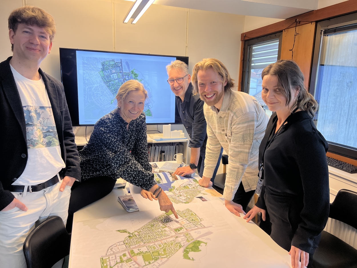 Byplanleggerne Eivind, Marit, Ubbo, Sven og Louise vil gjerne høre hva du syns om Hillevåg-planen! På bildet står de fem rundt et bord med kart over planområdet foran seg. 