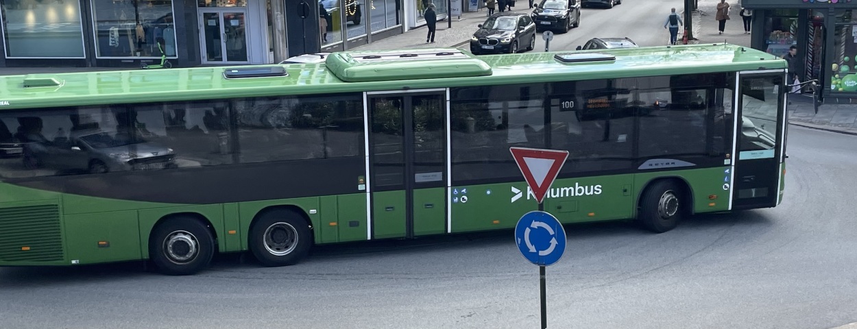 Grønn buss i rundkjøring, med biler i bakgrunnen.