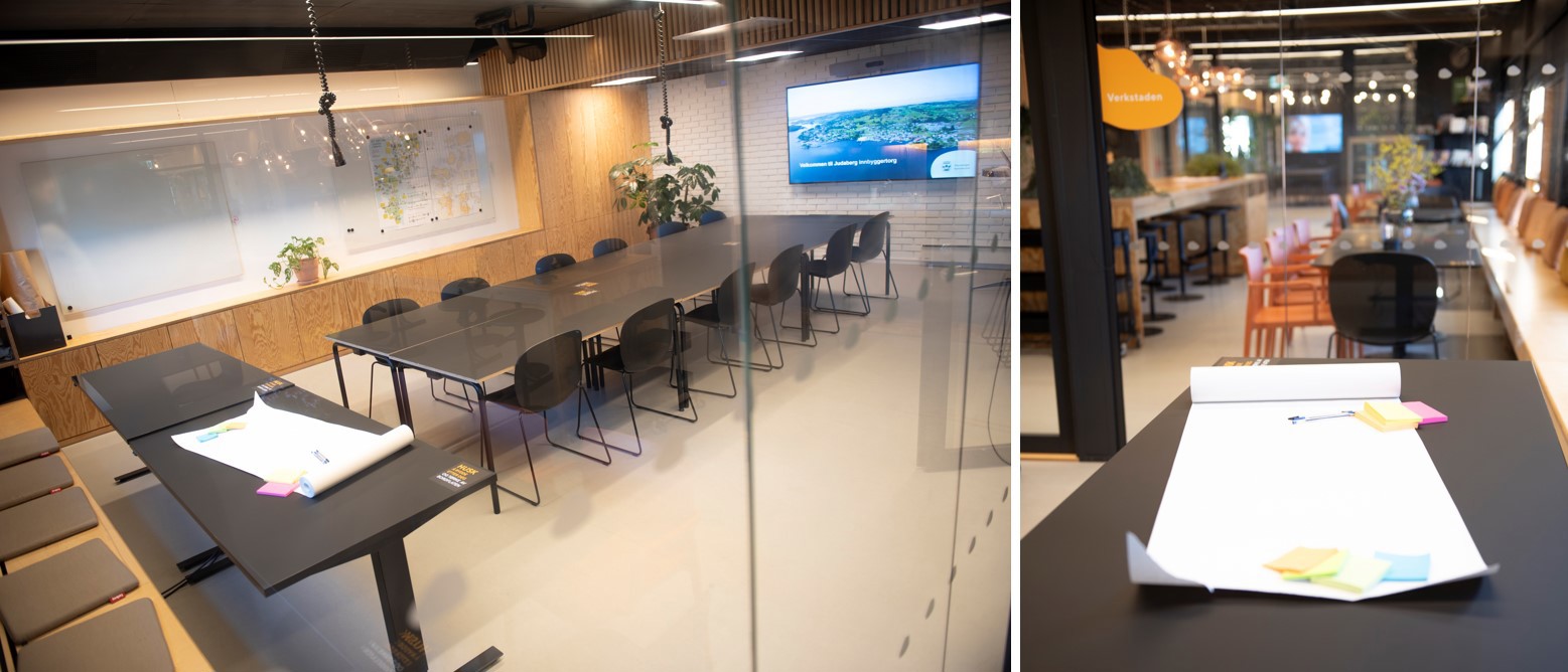 Stort møterom bak en glassvegg med møtebord, stoler, skjerm på vegg.