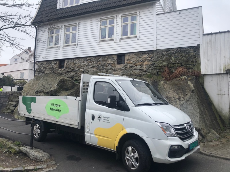 Bil i bymiljø med øyformer, logo og "Vi bygger fellesskap" på siden. 