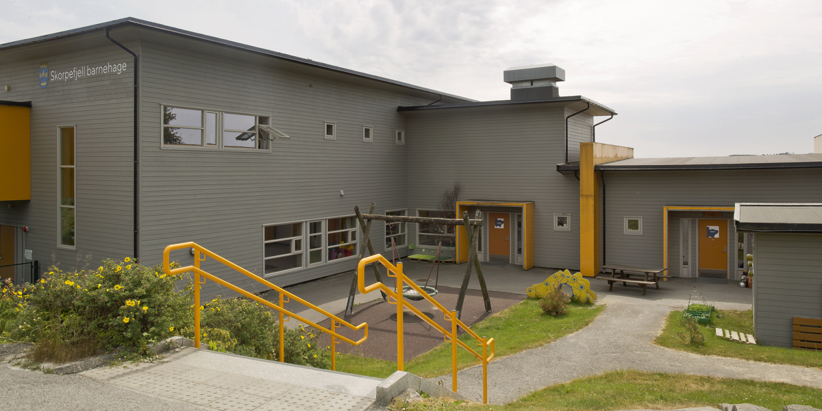 Barnehagebygg fra utsinden med uteplass med lekestativer