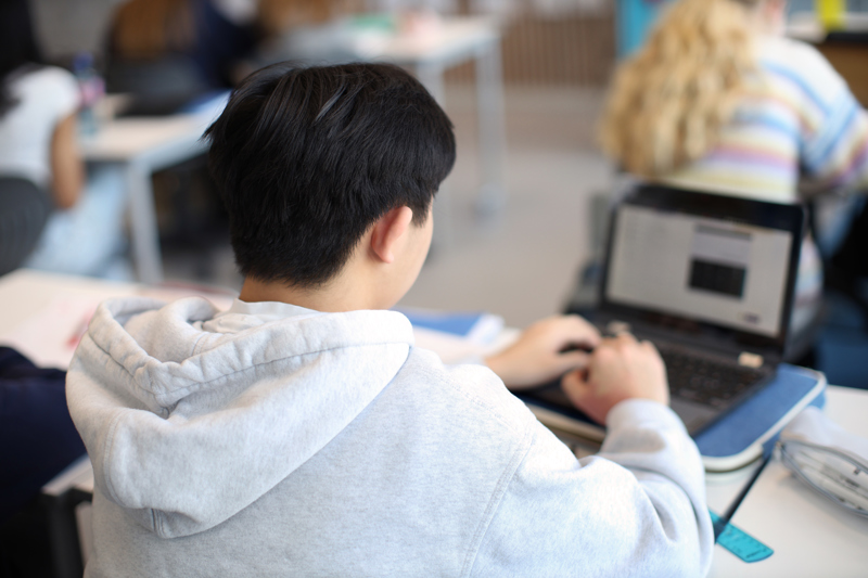 en elev sitter på en pult i klasserommet med ryggen til