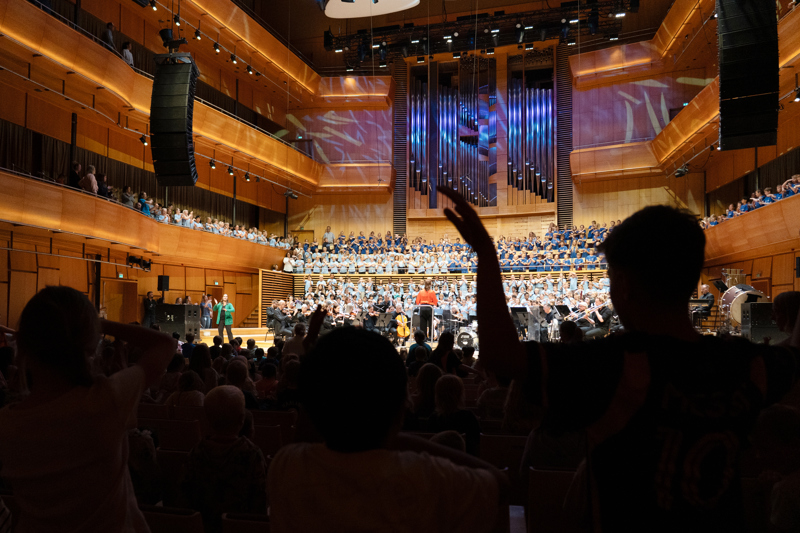 Mange barneskoleelever står på scenen i Stavanger konserthus og synger i samspill med Stavanger symfoniorkester.