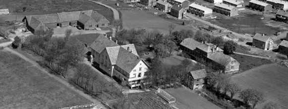 Flyfoto fra 1957 i svart-hvitt av et stort, ganske staselig gårdstun med store trær omkring. Rekkehus synes i utkanten av bildet.