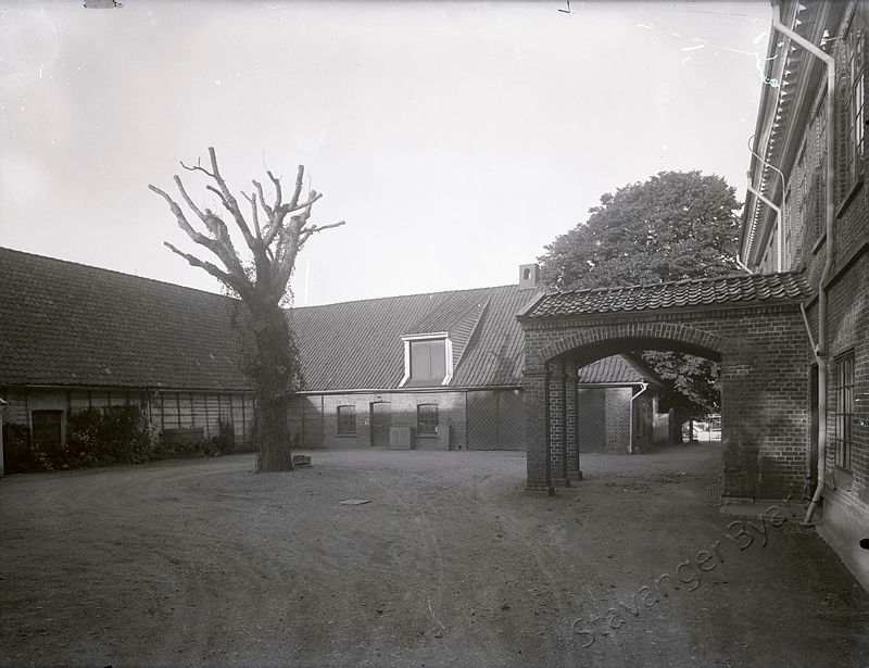 Svart-hvittbilde av gårdsrommet bak Ledaal, med portbygning, stall og tuntre.