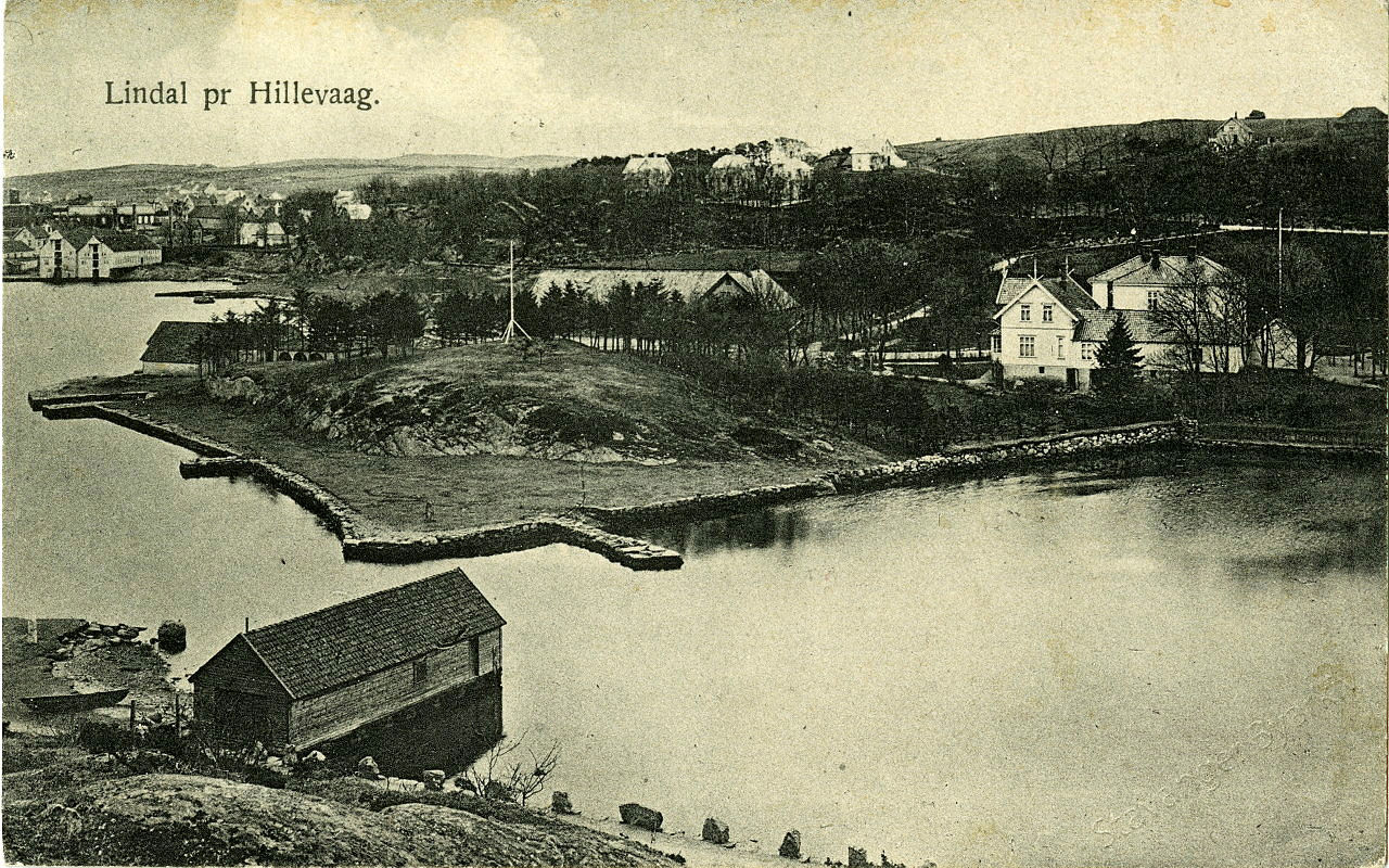 Baker Lindals lystgård, ved Hillevågsvannets sund mot Gandsfjorden, der Strømsbrua står i dag. Fra etpostkort fra Hillevåg, ca. 1900-1910. Foto: Byarkivets postkortsamling/Stavanger byarkiv Et svart-hvittbilde av en staselig gård ved vannet, med sjøhus og andre gårder i bakgrunnen.