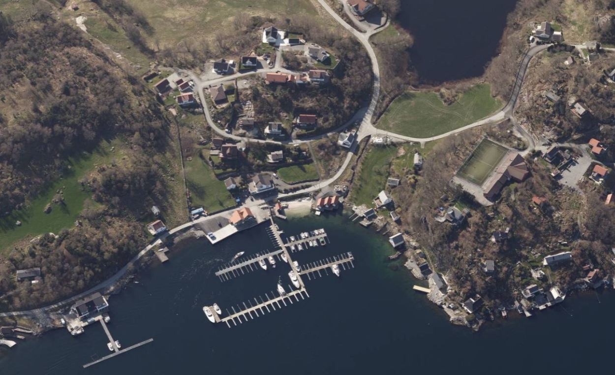 Flyfoto av Skardtveitvågen, med småbåthavn, sandstrand, landhandel, hytter og boliger.