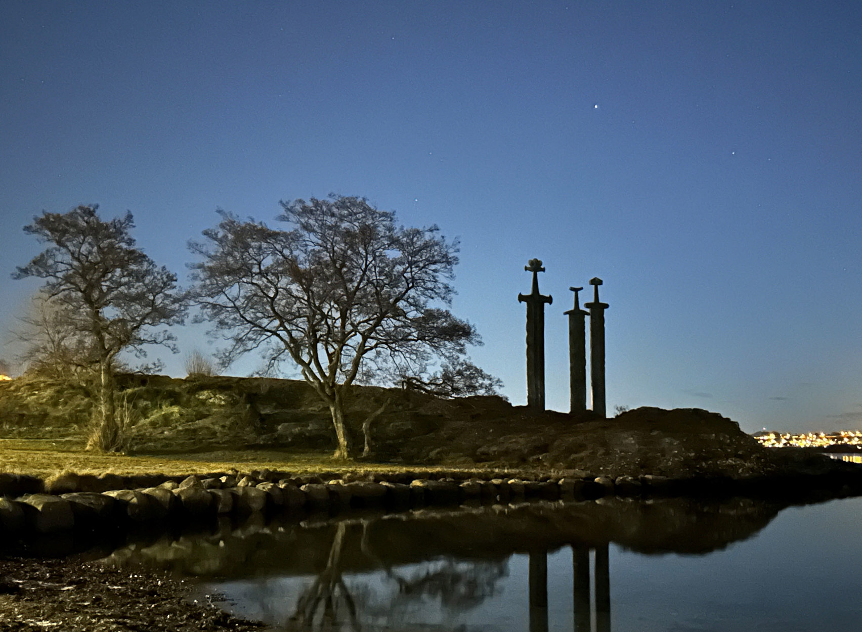 Skulpturen "Sverd i fjell" i solnedgang, med stjerner og lyskastere inn fra venstre.