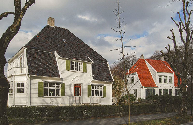 Stort, flott jugendhus med store takplater. Hvit kledning og grønne skodder. 