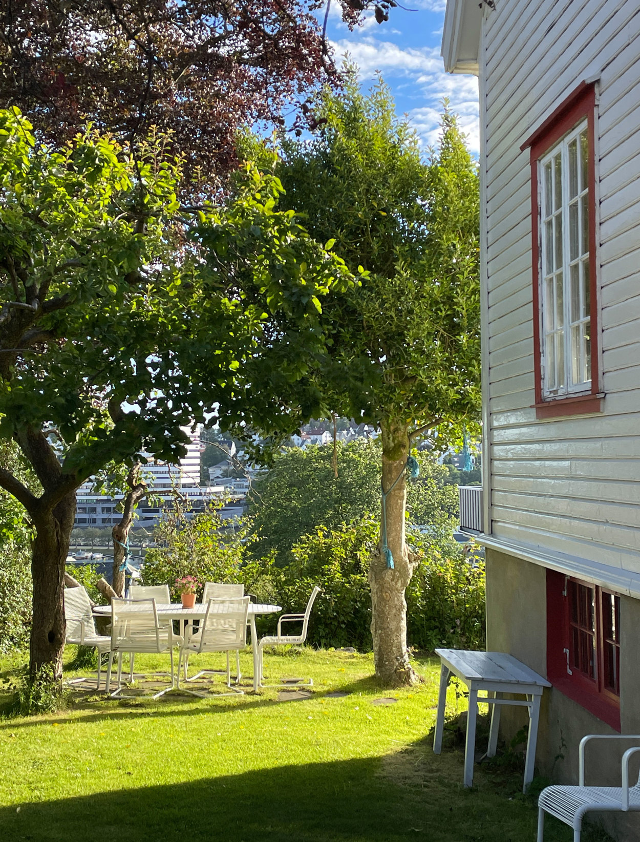 Bakhagen med plen, og sittegruppe under plommetreet.
