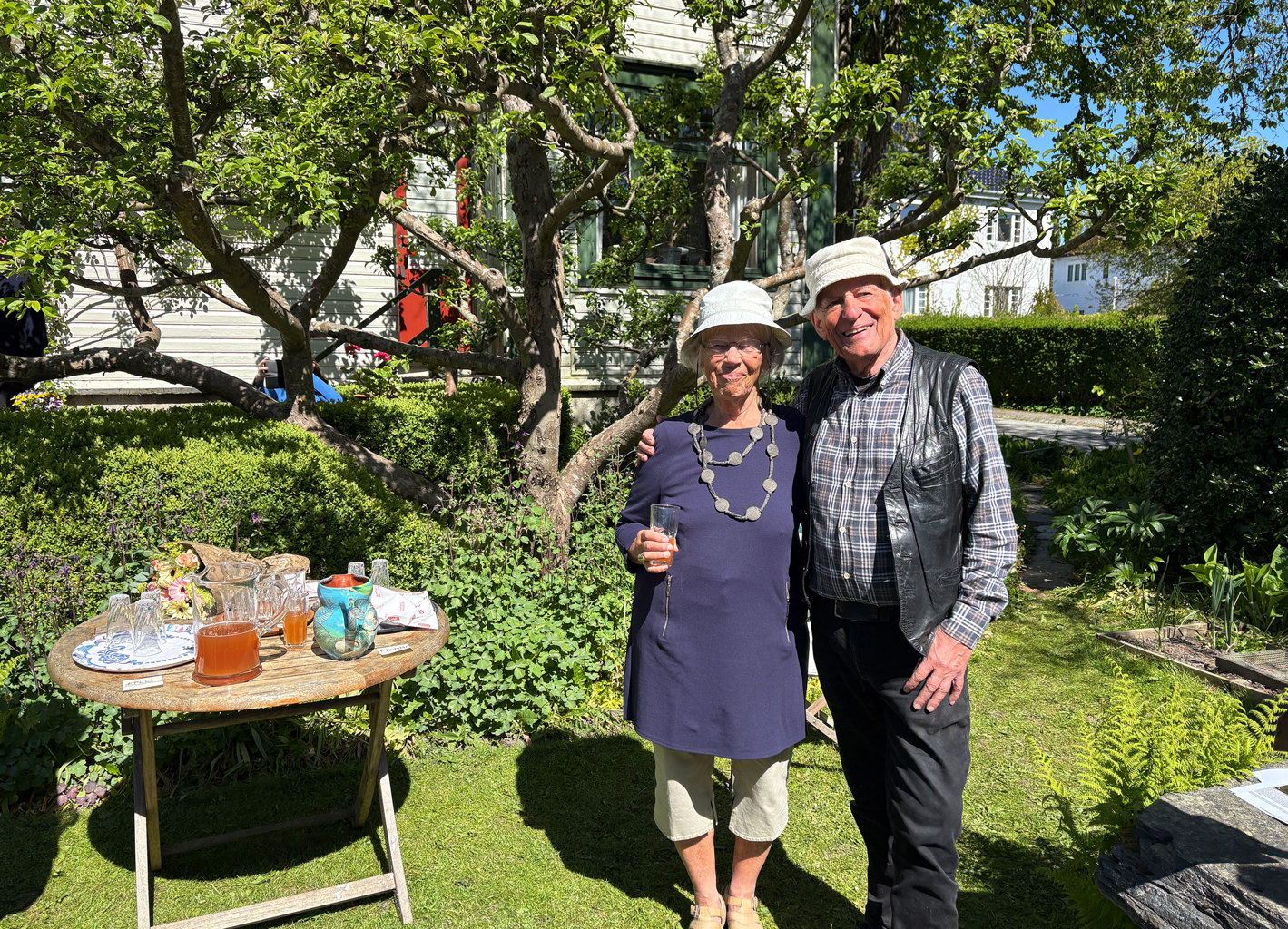 Elsa og Per Grimnes serverte eple- og plommesaft – selvfølgelig fra egen hage – under prisoverrekkelsen. Ektepar i hagen, foran et gammelt epletre.