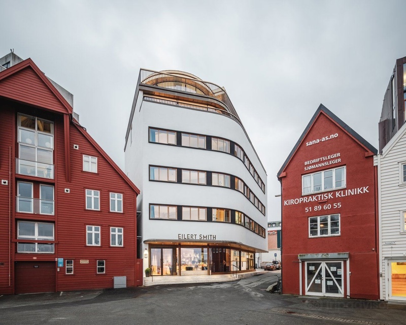 Funksjonalistisk hotellbygg med smekre linjer, mellom to røde sjøhus. 