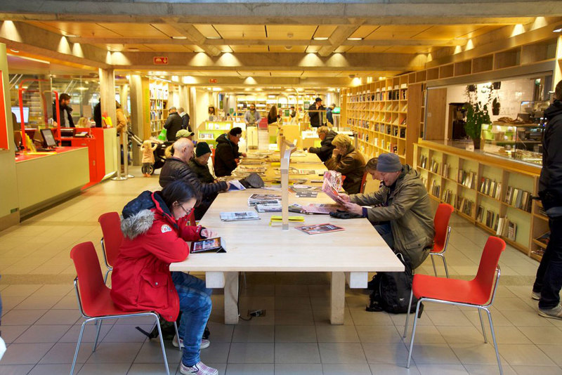 Aviskroken på biblioteket, folk sitter rundt et bord og leser aviser. 