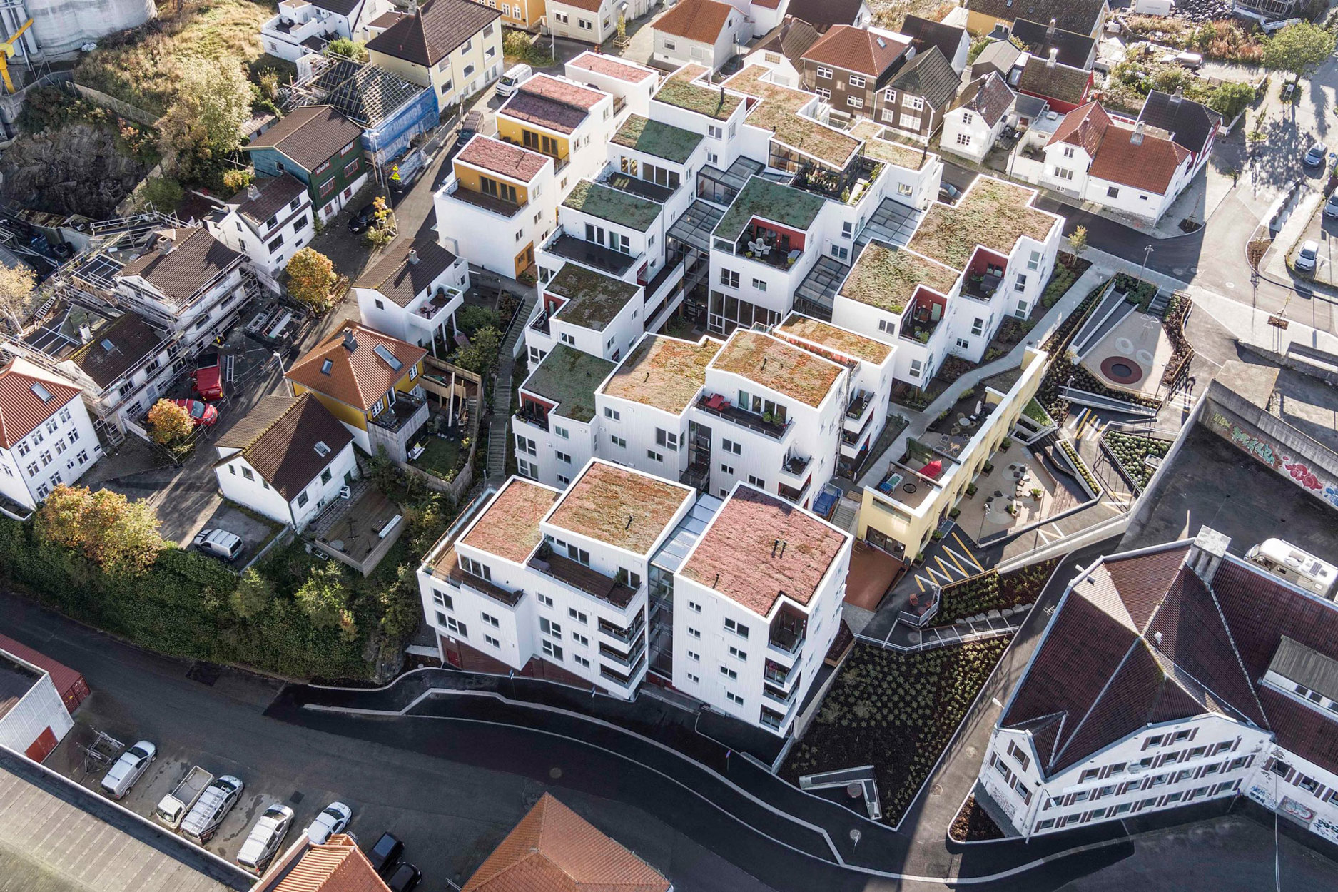 Dronebilde av Vindmøllebakken, som er utformet i volumer som tar opp skalaen i tilliggende småhus. Bofelleskapet, rekkehusene og leilighetsbygget har klar egenart og er samtidig beslektet med naboer i materialbruk og vinduer. Arkitekt: Helen & Hard.