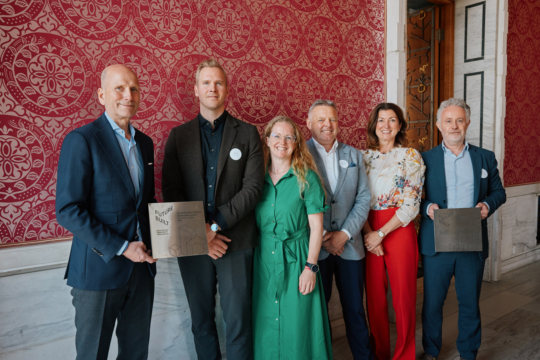 Fem pent kledde mennesker. To av dem holder opp en plakett det står "FutureBuilt" på.