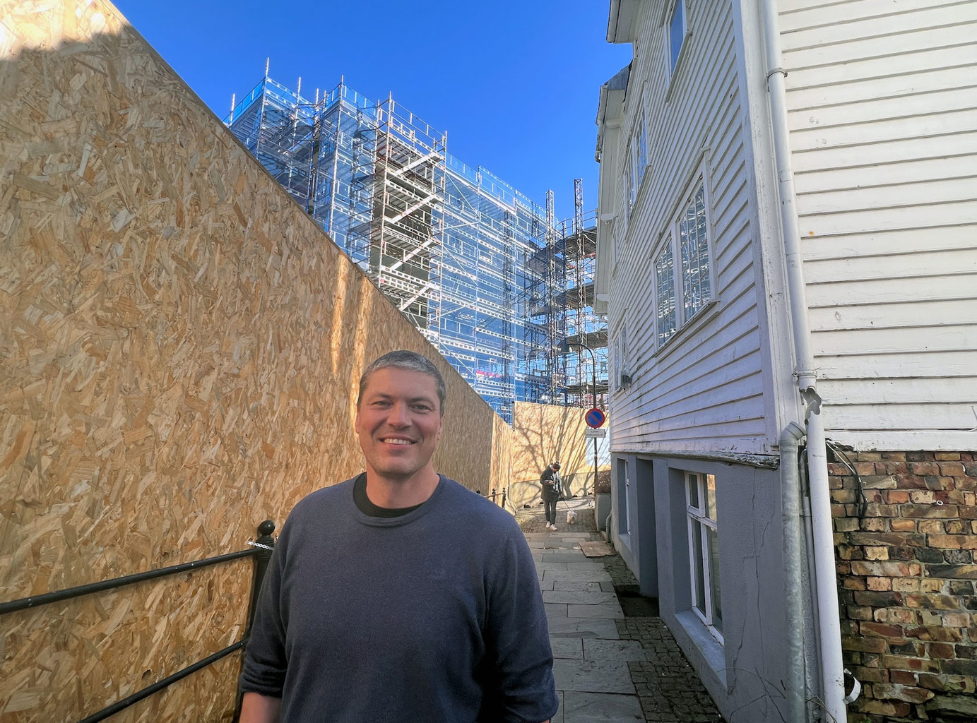 – Den nye byarkitekten skal inspirere, utfordre, tenke nytt og bidra til at vi sammen bygger en vakker by, sier byggesaksjef Sven Norland. Byggesaksjef Sven Norland står mellom et byggegjerde og et gammelt trehus, med et byggeprosjekt i bakgrunnen.