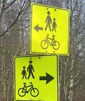 To gule skilt med svarte piler som viser omvei for syklister og fotgjengere.