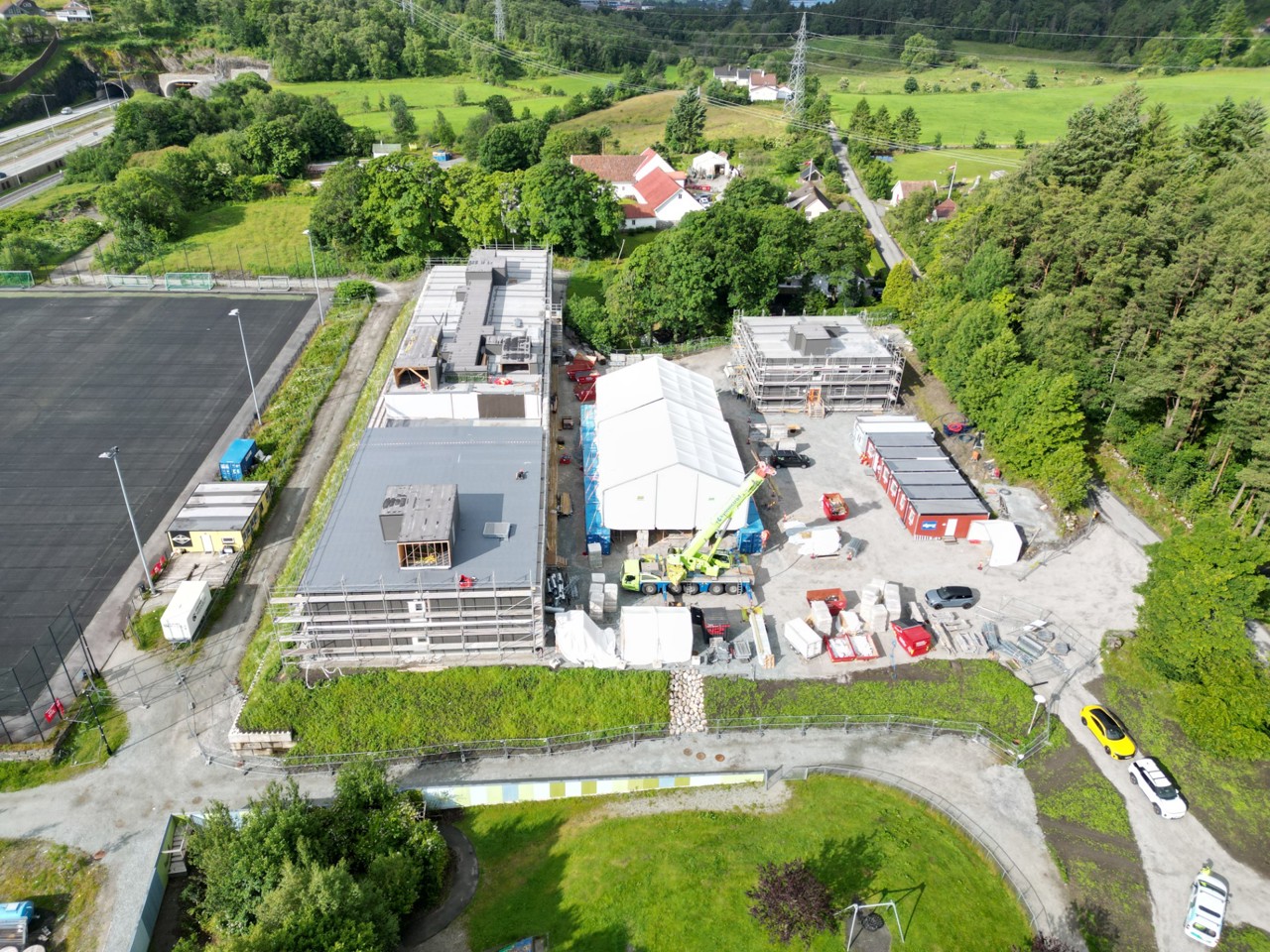 Byggeplassen for den midlertidige Vaulen skole, juni 2025. Byggeplass med skolebygg, byggetelt og brakker, omkranset av trær, kulurlandskap og fotballbane.