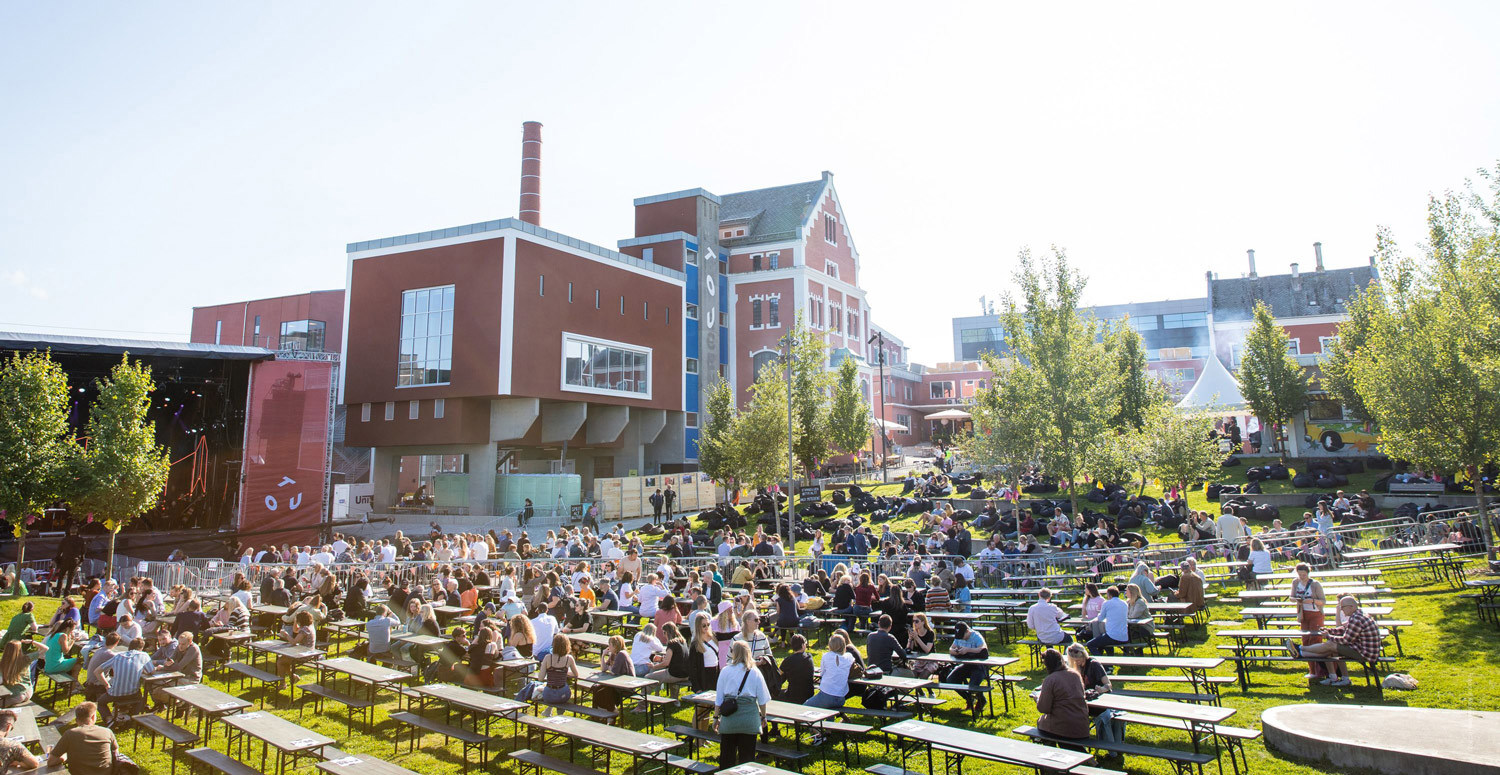 Utekonsert en sommerdag i parken ved Tou, med masse folk som sitter langs piknik-bord.