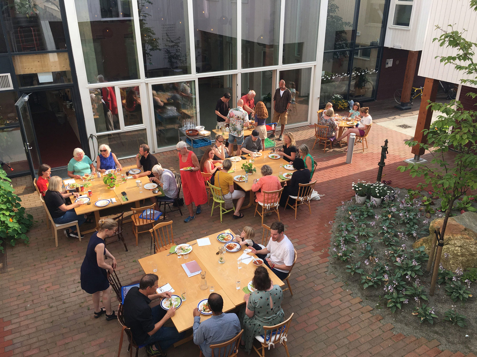 Folk som sitter og spiser rundt flere bord i gårdsrom. Foto: Siv H. Stangeland