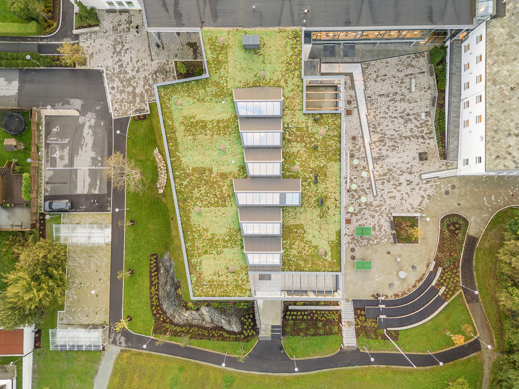 Dronebilde av bygget ovenfra. Rombehovet for tilbygget var opprinnelig rundt 3000m2, men arkitektene fant nye løsninger som gjorde at halvparten av rombehovet kunne få plass i eksisterende bygg. Ved å redusere nybyggbehovet til halvparten oppnås en betydelig miljøgevinst. Det er fulgt opp ved at nybygget er gjennomført med høy miljøprofil.