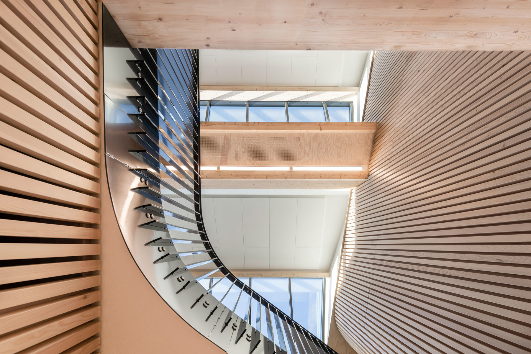 Nærbilde av vegger med spiler i tre, og en trapp med organiske former. Det er en generøs og lettlest romlighet som en vakker ramme for de unges sosiale fellesskap, et godt sted for læring og en attraktiv arbeidsplass.