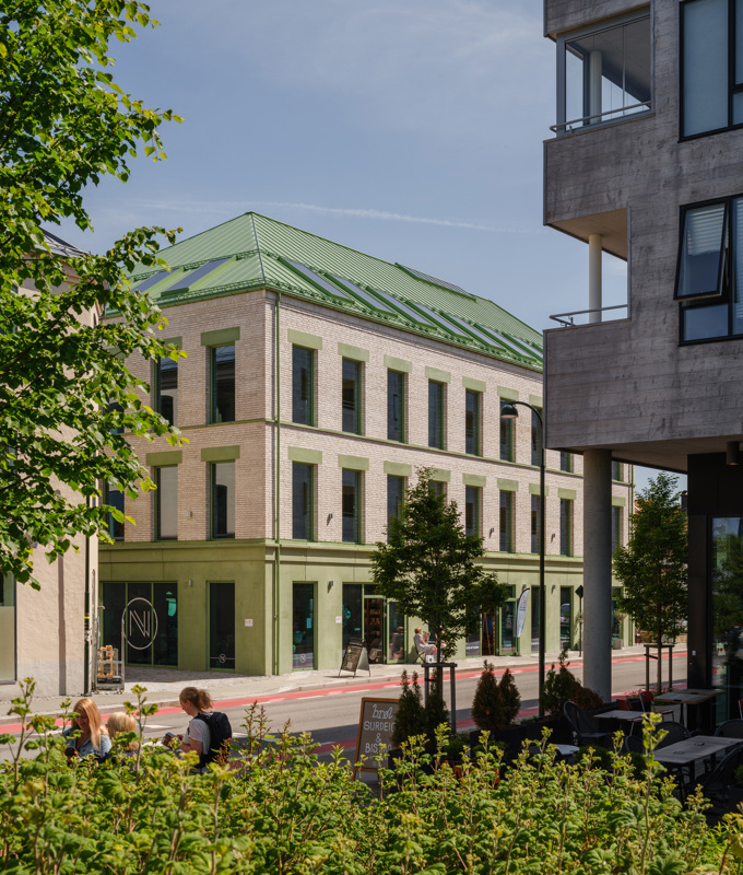 Murbygning med grønnfarget betong i første etasje, og butikkvinduer. Rødt sykkelfelt langs gaten utenfor. 