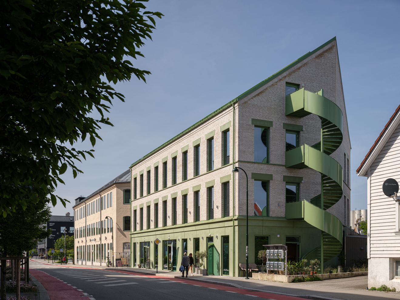 Murbygning med tegl og grønne betongelementer, og en særegen, grønn rømningstrapp i gavlen.