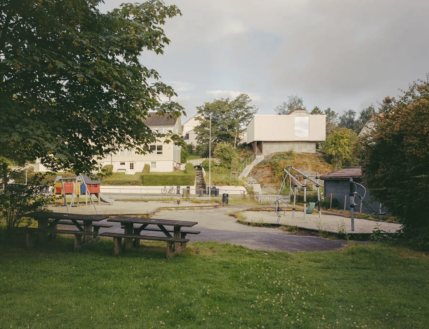 Lekeplass i forgrunnen. Det nominerte huset ligger på et berg i bakgrunnen, med trapp ned til gaten.