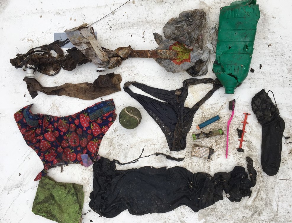 Skittent avfall som er hentet opp fra avløpsvann i kloakkrør ligger på et hvitt underlag. En liten ball, en truse, en sokk, plastemballasje, en ødelagt flaske, en lighter med mer.
