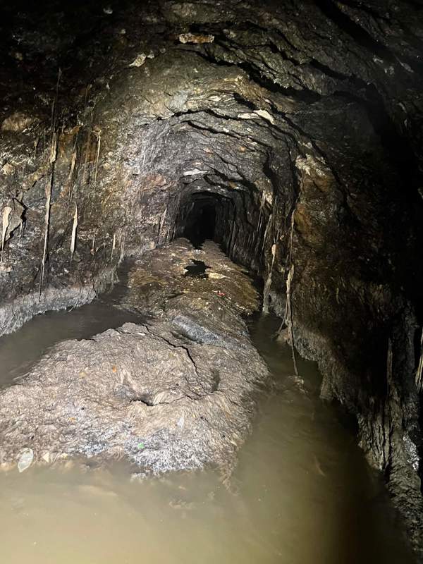 Et langt grått berg av slimete søppel ligger innover i en mørk tunell, halvveis nede i kloakkvann som siger forbi. papir og avfall har hengt seg opp i den knudrete veggen, i søppelberget skimtes blant annet en kondom.