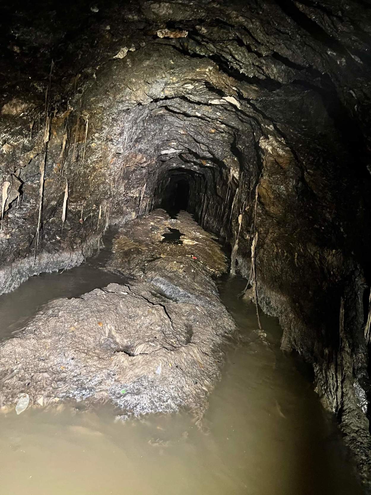 Et langt grått berg av slimete søppel ligger innover i en mørk tunell, halvveis nede i kloakkvann som siger forbi. papir og avfall har hengt seg opp i den knudrete veggen, i søppelberget skimtes blant annet en kondom.