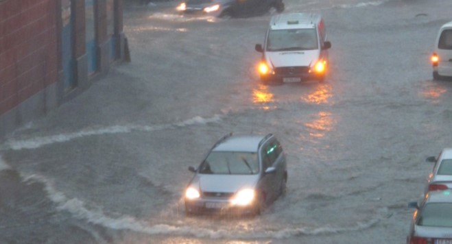 København etter massivt skybrudd i 2011. Foto: Magnus Manske / Creative Commons, https://commons.wikimedia.org/wiki/File:Istedgade_skybrud_2011-07-02.jpg. Gjengitt med tillatelse i Creative Commons Attribution-Share Alike 2.0 Generic license. Biler kjører gjennom et lyskryss i København, og det er vann opp over hjulene etter ekstrem nedbør.