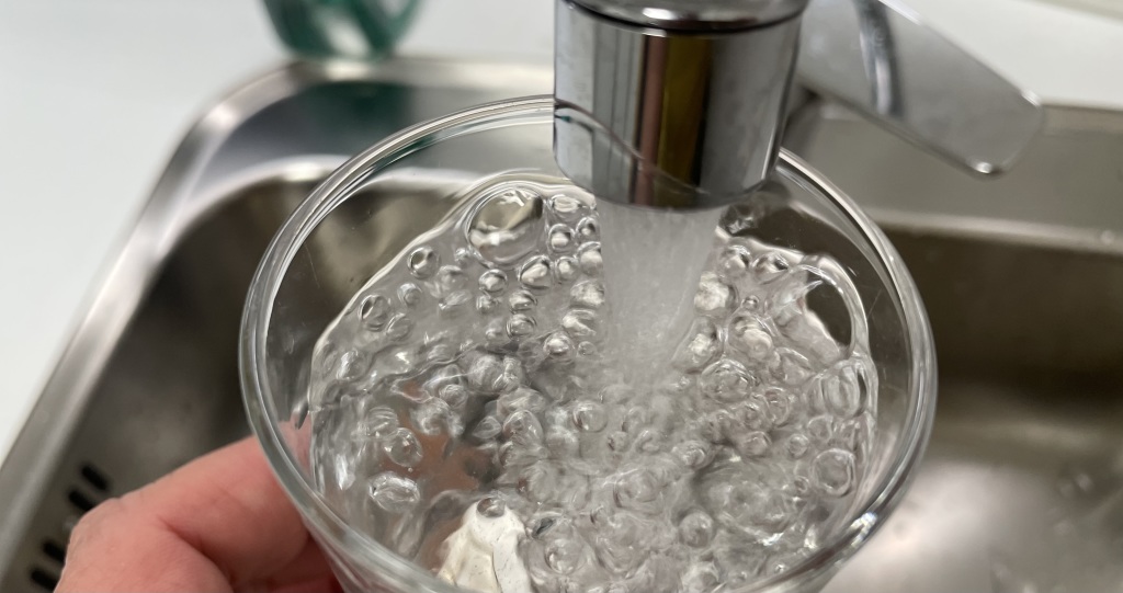 Nærbilde av vann som strømmer fra springen ned i et glass.