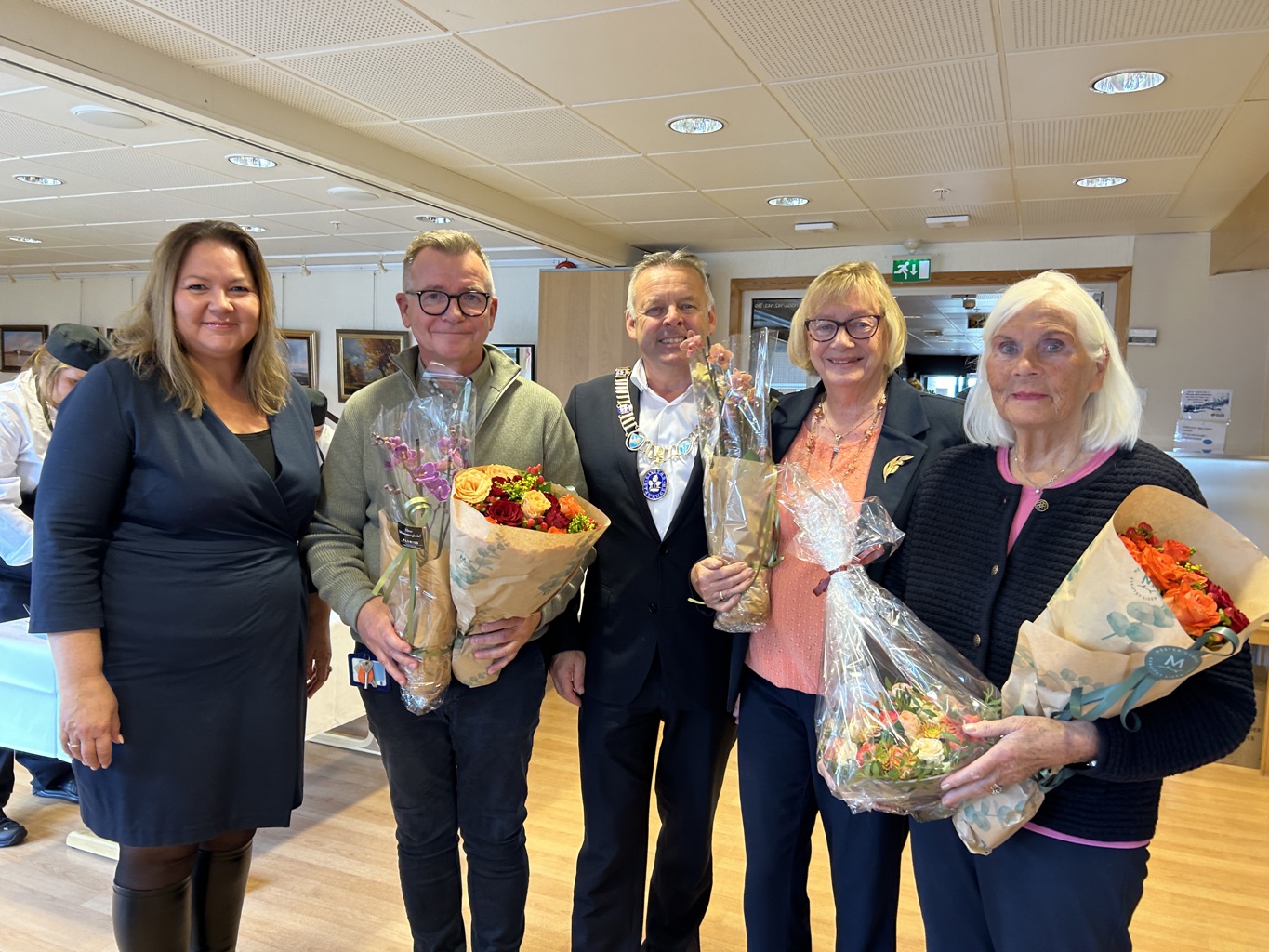 BLOMSTER OG GODE ORD: F.v. direktør helse og velferd Stina Løkke, virksomhetsleder Rune Ludvigsen, fungerende ordfører Henrik Halleland, eneste gjenværende av husmorlagene som dannet Stiftelsen Øyane sykehjem Ingunn Thorsen og driftsstyreleder og leder for stiftelsen Olaug Tveit Pedersen. Fire personer står ved siden av hverandre inne på Øyane sykehjem med smilende fjes og blomster i armene.