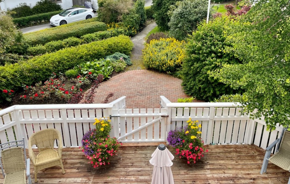 Bildet  viser utsikten ned i hagen fra balkongen i andre etasjen. Med blomsterkrukker og grønne busker i hagen.