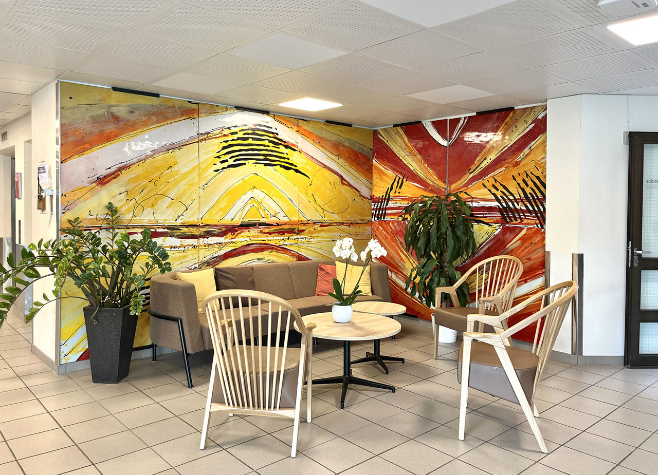 Vi ser en fin sittegruppe med sofa, stol og bord som står i resepsjonen på sykehjemmet. Det er et stort bildet i gule og røde farger bak.