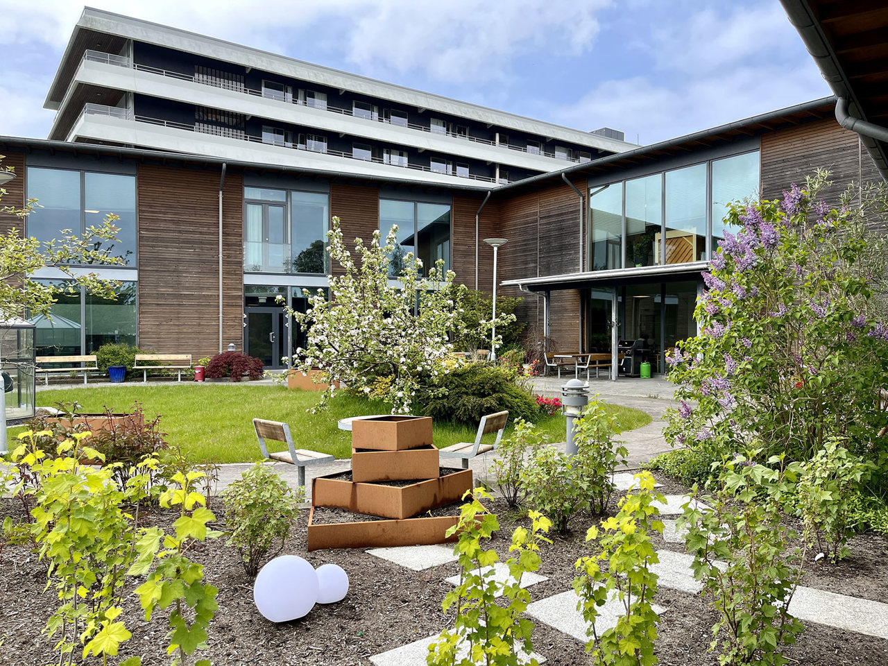 Bildet viser en hage mellom byggene til demensavdelingen. Vi ser busker, plantekasser og belysning.