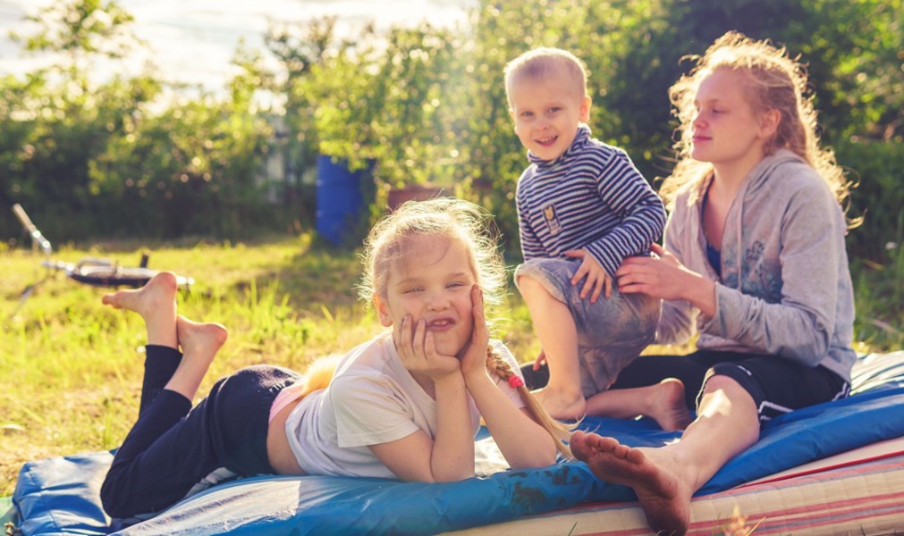 Tre barn på et pledd på en mark en fin sommerdag
