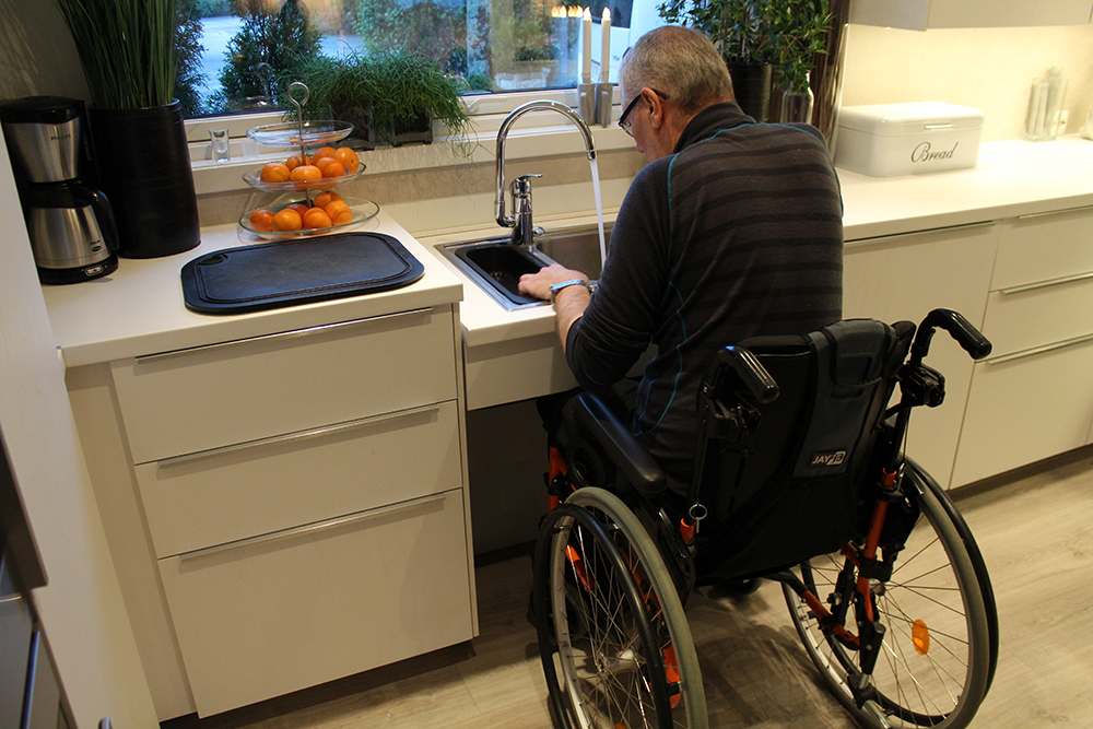 Mann i rullestol ved kjøkkenbenk og vask som er i tilpasset høyde.