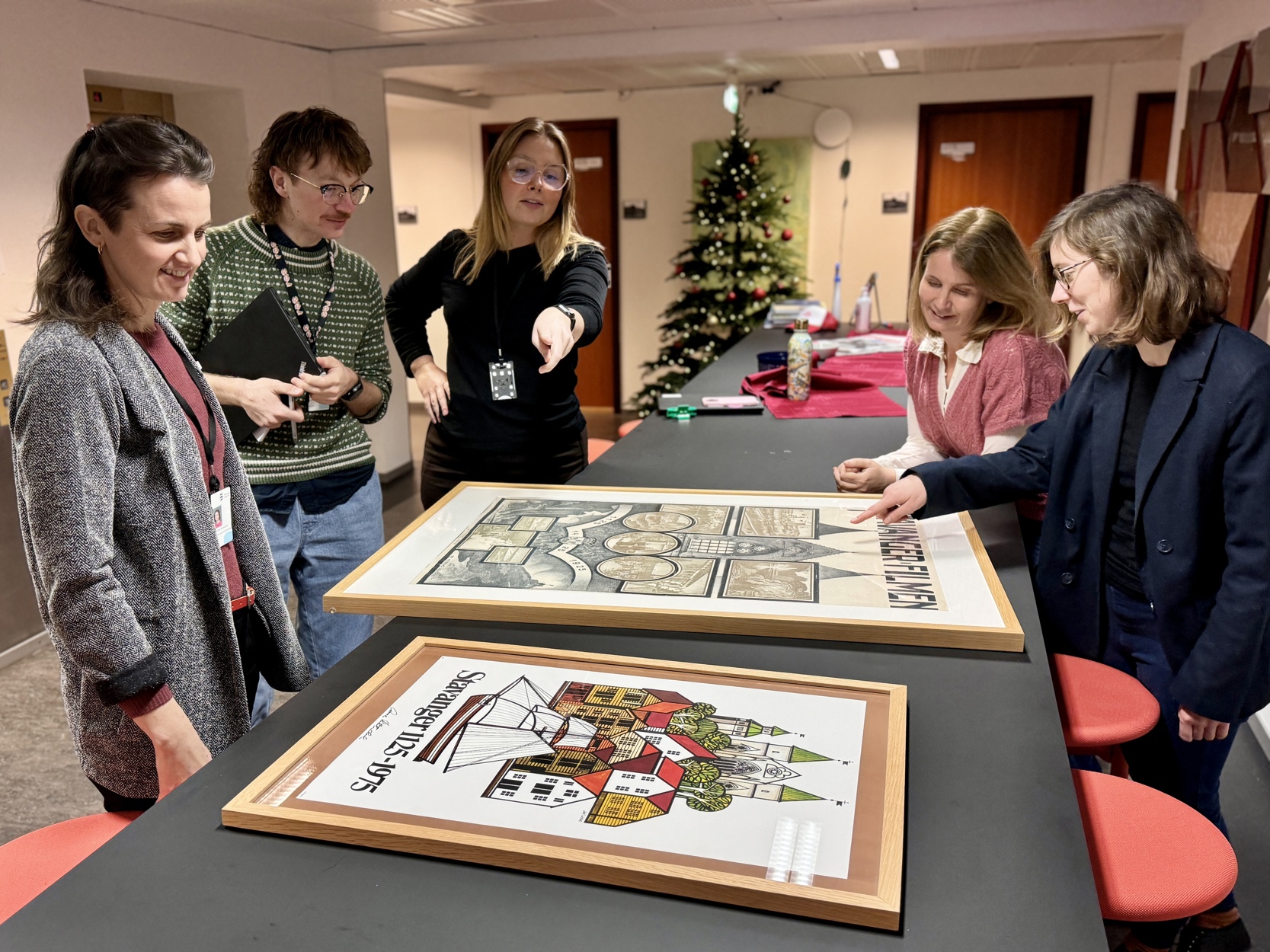 Juryen står rundt et bord og diskuterer jubileumsplakaten fra 1975.