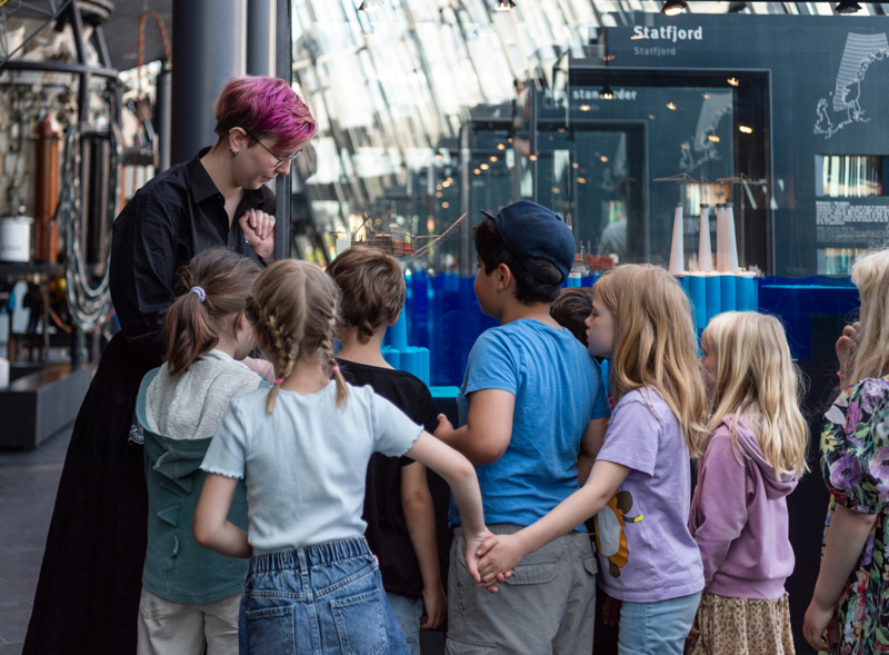 Voksen kvinne som forklarer noe til små barn på et museum. 