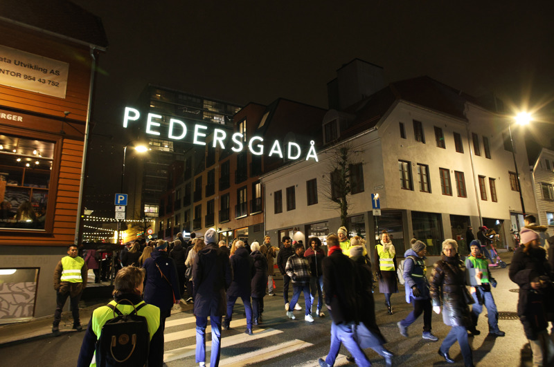 Flere mennesker vandrer i Pedersgata under skiltet hvor det står "Pedersgadå"