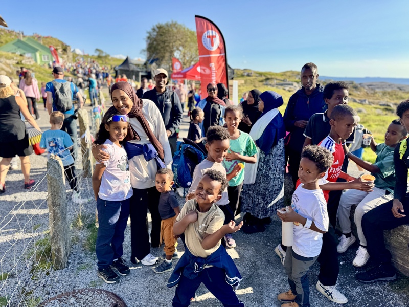 Voksne med mange barn smiler og ler i kamera. 