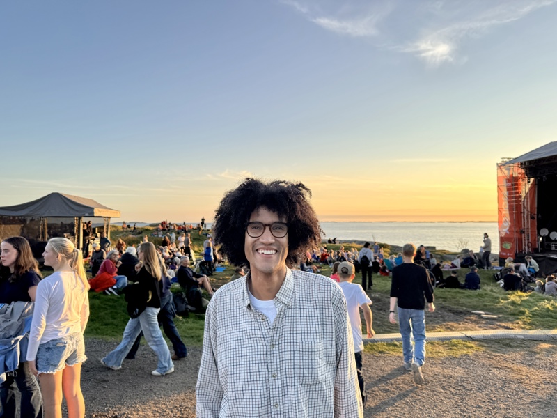 Beharie smiler til kamera. I bakgrunnen er nydelig natur og en begynnende solnedgang. 