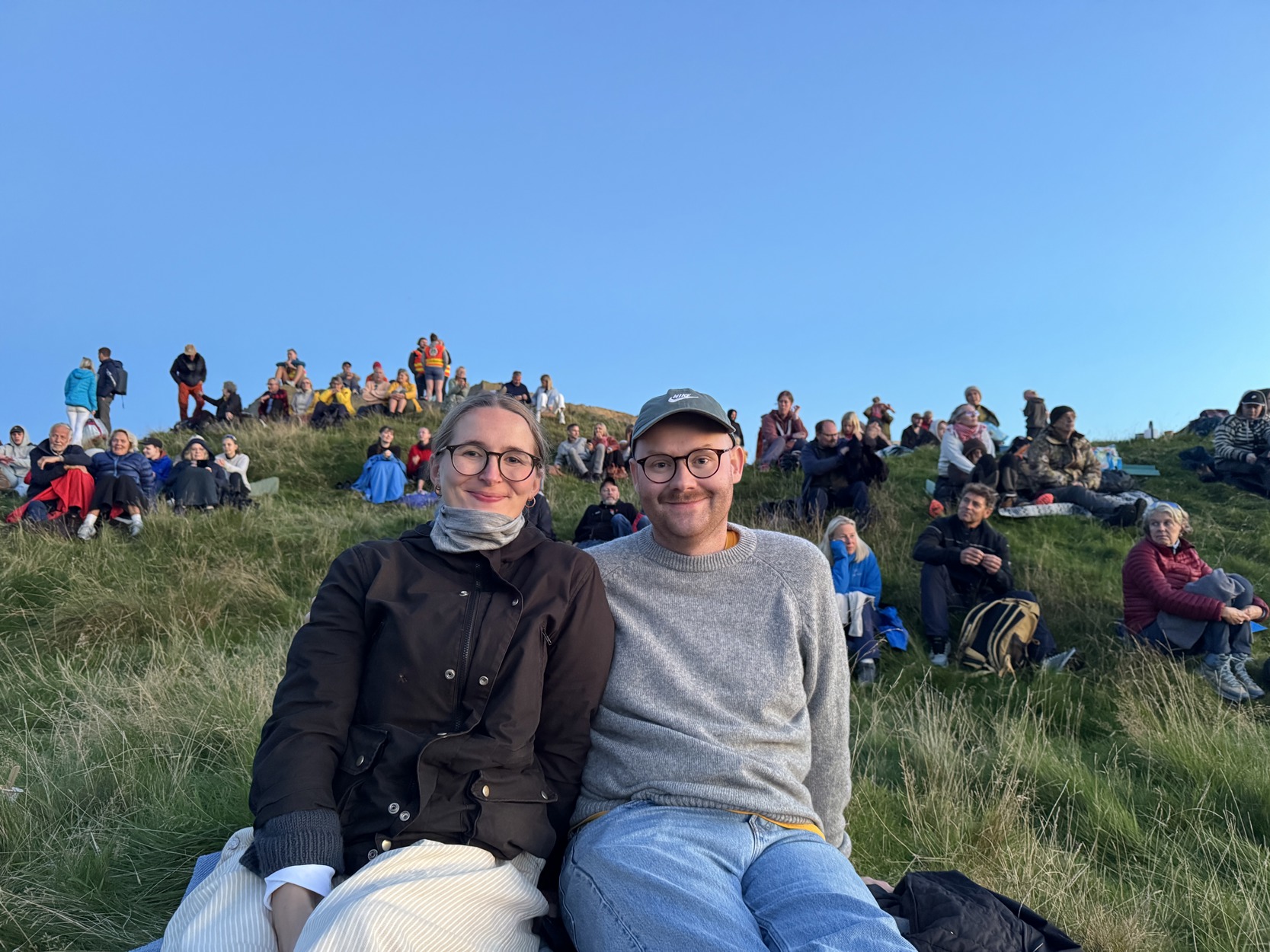 En kvinne og en mann smiler i kamera. Bak dem sitter flere mennesker.