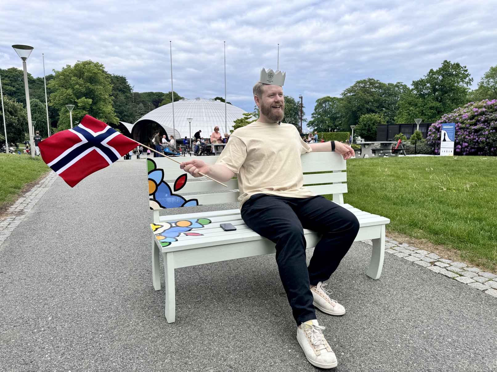 Mann sitter på benk i bjergstedparken, med flagg og krone.